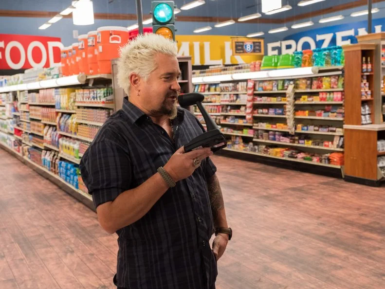 Host Guy Fieri speaks into the intercom, as seen on Food Network's Guy's Grocery Games, Season 12.