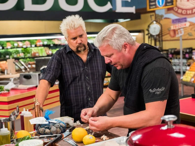 Host Guy Fieri checks in on contestant Adam Sappington as he sparates a garlic bulb, as seen on Food Network's Guy's Grocery Games, Season 12.