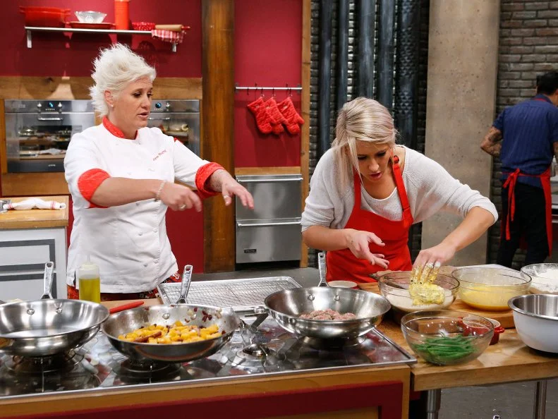 Mentor Anne Burrell helps Mandy Thornton of the red team as she cooks during the main dish challenge, as seen on Food Network's Worst Cooks in America, Season 10.