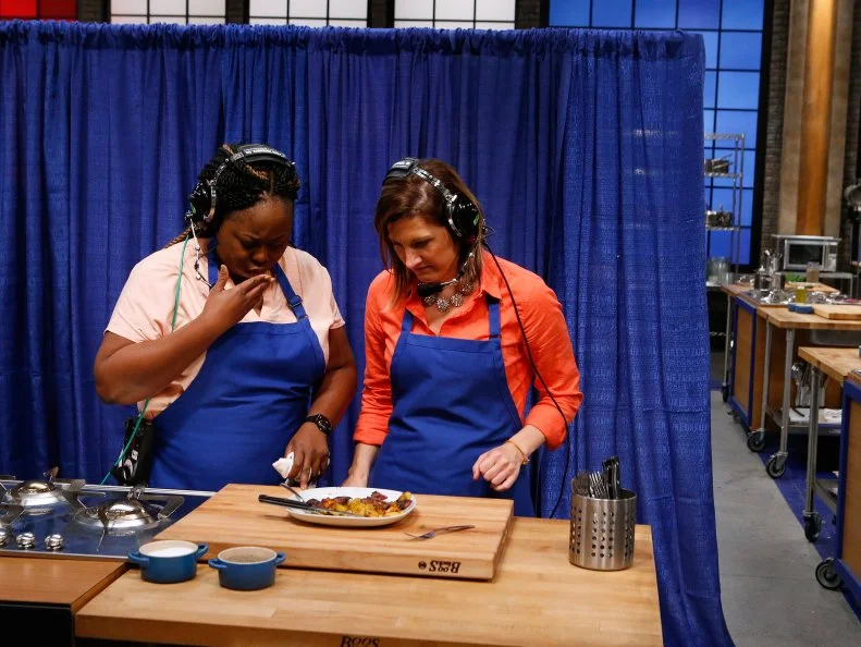 Ann Odogwu and Laura Docker of the blue team guide mentor Rachael Ray through the preparation of a dish via headset only during a game of Remote Control Chef, as seen on Food Network's Worst Cooks in America, Season 10.