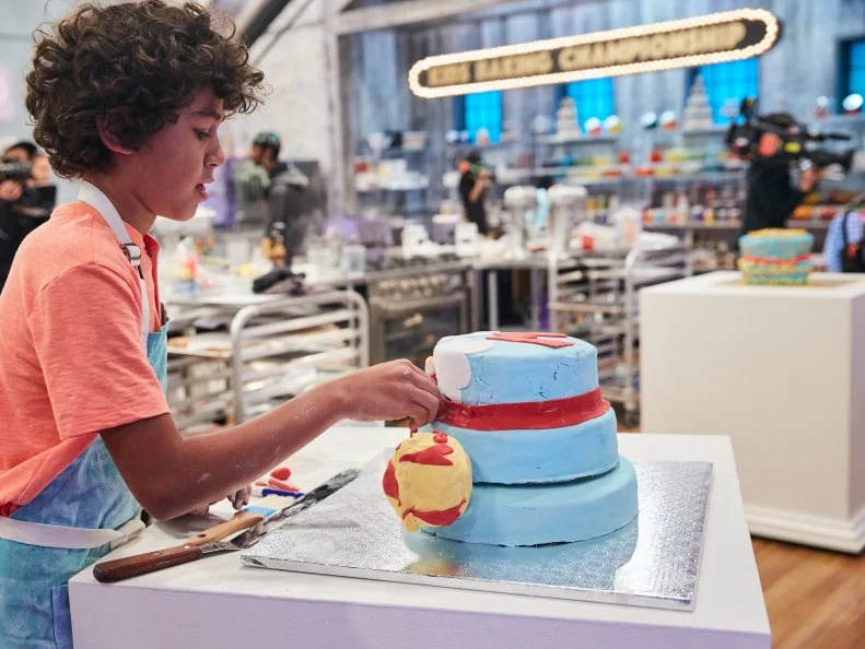 Contestant Justice Faustina preparing his Main Heat dish, Rose Flavored Cake with Vanilla Buttercream and a Rice Cereal Treat Villain, with Weather Man as the Superhero and Mr. Sun as the Villain, as seen on Food Network's Kids Baking Championship, Season 3.