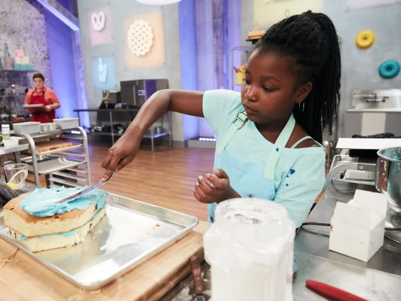 Contestant Kaniyah Car preparing her Main Heat dish, Lemon Blueberry Cake with Lemon Buttercream, Sandwich Cookie Villain and a Vanilla Buttercream Super Hero, with Catastrophe Girl as the Superhero and Mr. Potato as the Villain, as seen on Food Network's Kids Baking Championship, Season 3.