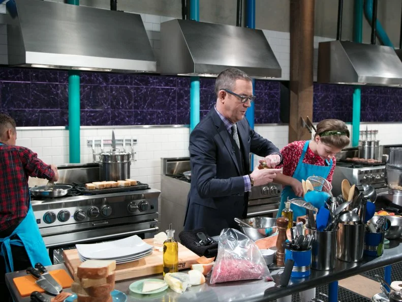 Host Ted Allen with Junior contestant Nicole Bidun as she cooks Taleggio burger with Belarussian apples and stained glass basil during the entrŽe round, as seen on Food Network's Chopped Junior, Season 6.