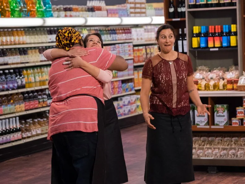 Contestants Michael Marina and Kate Newman hug while Tracey Shepos gives a shocked expression, as seen on Food Network's Guy's Grocery Games, Season 12.