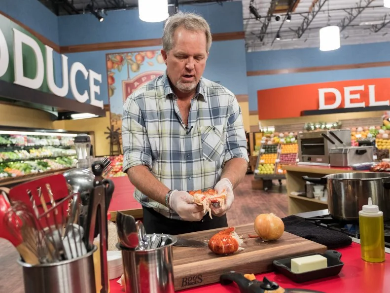 Contestant John Conley pulls apart a lobster tail while preparing his dish, as seen on Food Network's Guy's Grocery Games, Season 12.