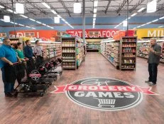 Contestants Glenn "Gator" Thompson, Tracey Sherpos-Cenami, Samuel Monsour, and Tom Ramsey listen as Host Guy Fieri explains the rules for the 20 Minutes or Less game, as seen on Food Network's Guy's Grocery Games, Season 12.