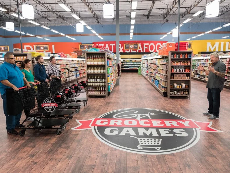 Contestants Glenn "Gator" Thompson, Tracey Sherpos-Cenami, Samuel Monsour, and Tom Ramsey listen as Host Guy Fieri explains the rules for the 20 Minutes or Less game, as seen on Food Network's Guy's Grocery Games, Season 12.