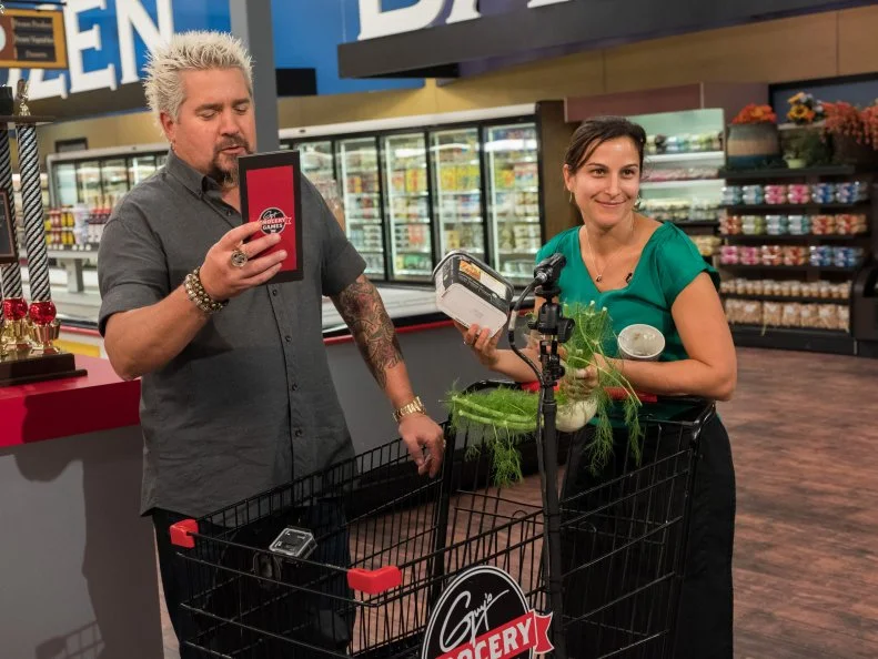 Host Guy Fieri instructs Contestant Tracey Shepos-Cenami while she plays the final shopping cart challenge, as seen on Food Network's Guy's Grocery Games, Season 12.