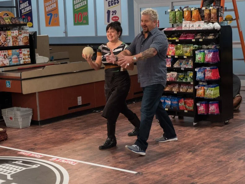 Contestant Lisa Kagen takes a lesson in bowling from Host Guy Fieri as she prepares to play the Grocery Bowl game, as seen on Food Network's Guy's Grocery Games, Season 12.