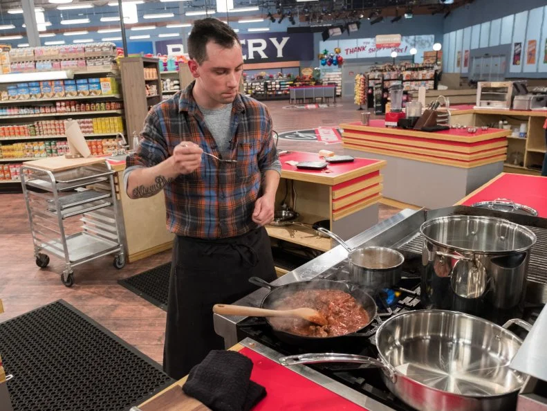 Contestant Lewis Leiterman samples the contents of his pan, as seen on Food Network's Guy's Grocery Games, Season 12.