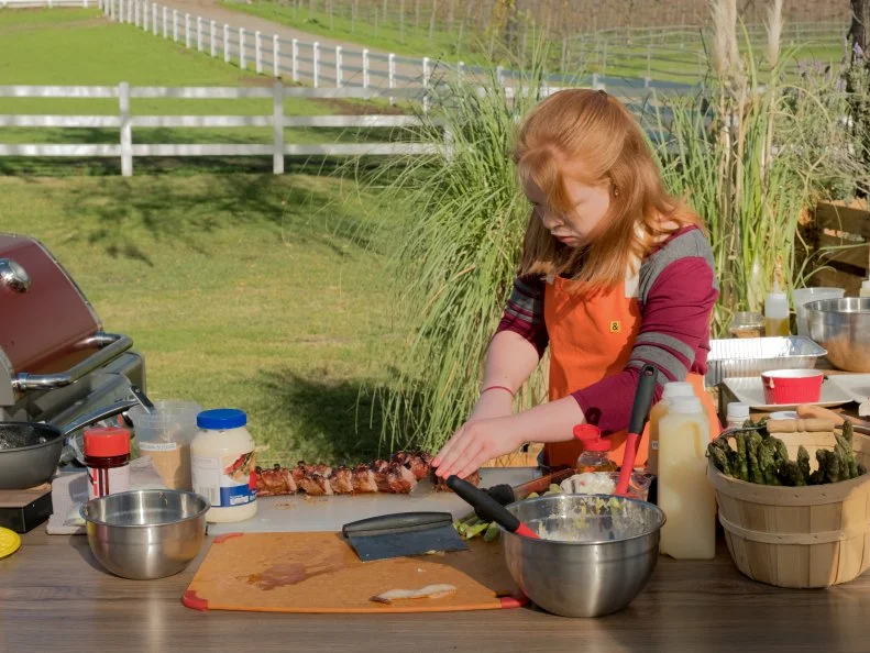 Contestant Allyson Keim cuts her baby back ribs for the main challenge Pig 3 Ways + Fruit, as seen on Kids BBQ Championship, Season 2.