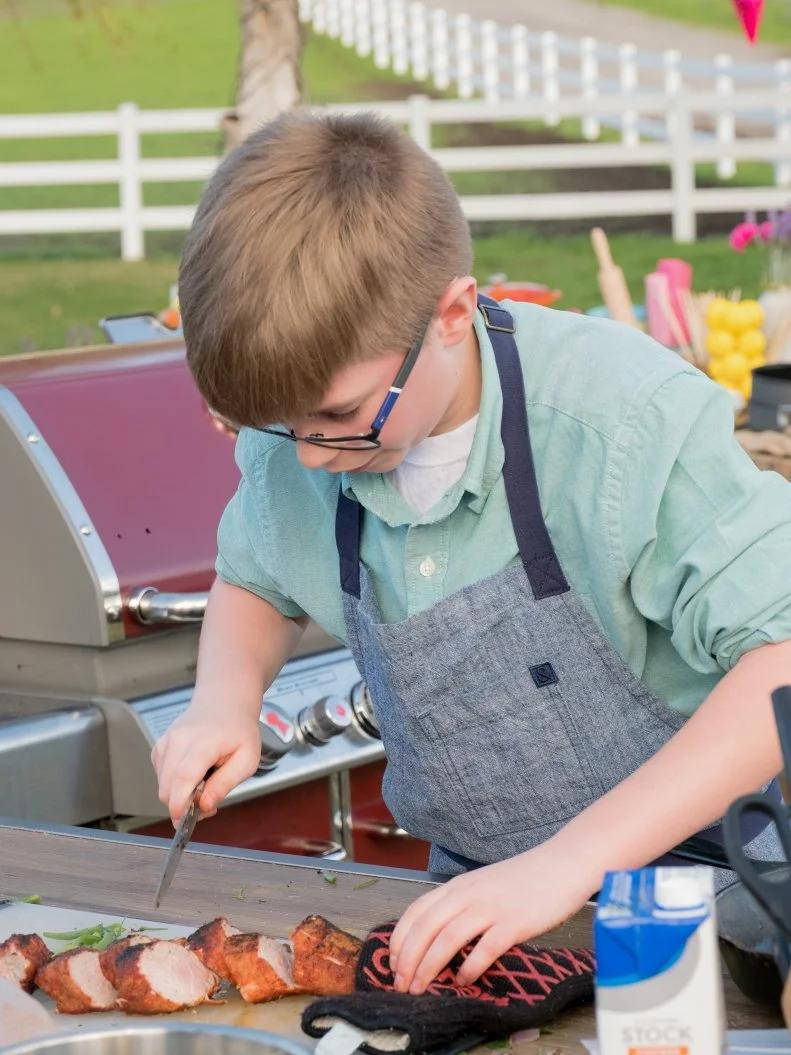 Contestant Hayden Wood cuts his pork tenderloin for his main challenge dish Hayden's BBQ Pork Tenderloin w/ Grilled Peach & Cilantro Salsa with Pancetta Green Beans, as seen on Kids BBQ Championship, Season 2.