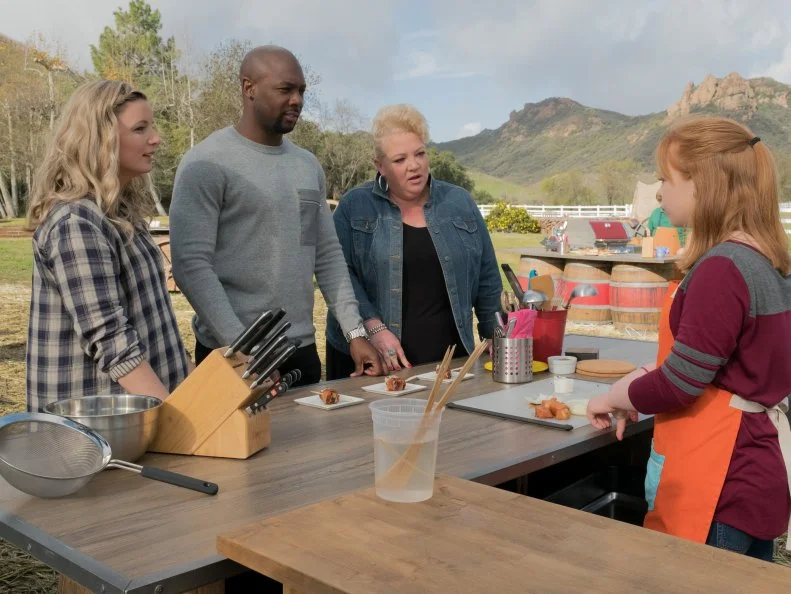 Host Damaris Phillips, Host Eddie Jackson and guest judge Diva Q samples contestant Allyson Keims Rooster Bullets (Bacon wrapped pork chop bites) with Stuffed Grilled Mushrooms, as seen on Kids BBQ Championship, Season 2.
