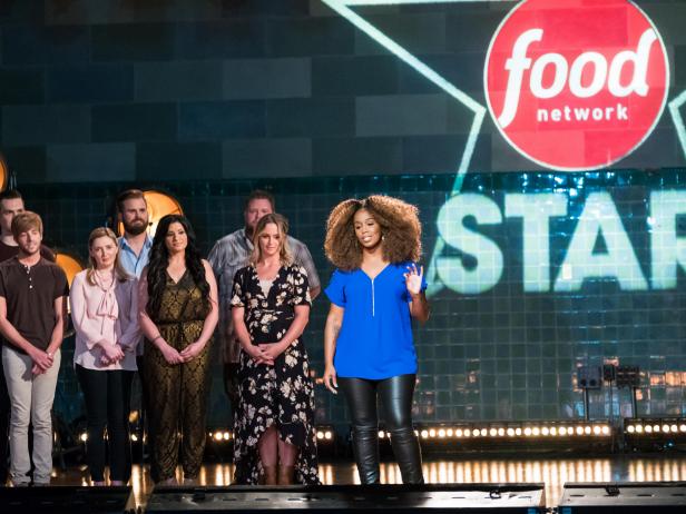 Contestants (left) Blake Bladwin, Trace Barnett, Addie Gundy, Cory Bahr, Suzanne Lossia, Rusty Hamlin and Amy Pottinger (right) behind contestant Toya Boudy introducing herself for the Mentor Challenge, Ready, Set...Rehearse!, as seen on Food Network Star, Season 13.