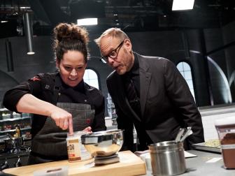 Host Alton Brown watches Chef Stephanie Izard preparing her dish, Cheese Plate (Blue Cheese Ice Cream with Blue Cheese Caramel Sauce, Bittersweet Chocolate Parmesan Crunch and Pickled Beet Tapenade), for the Cheese Battle, as seen on Iron Chef Gauntlet, Season 1.
