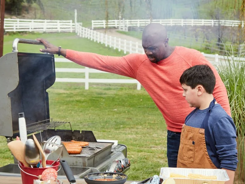 Host Eddie Jackson watches Contestant Daniel Marcus preparing his Round 2 dish, Daniel’s Crazy Clam Bake, as seen on Kids BBQ Championship, Season 2.