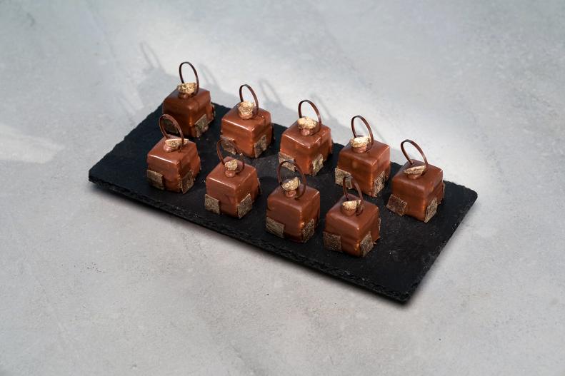Contestant Adam Young's dish is Cooked Milk Chocolate Sponge, with Caramel Pralines, Espresso Butter Cream, and Amoretto Gnash, during the Master Challenge, Mind Bending Cakes, as seen on Best Baker in America, Season 2.