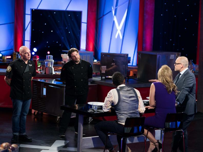 Contestant David LeFevre and Iron Chef Michael Symon stand in front of Judges Marcus Samuelsson and Donatella Arpaia with host Alton Brown, as seen on Iron Chef Gauntlet, Season 2.