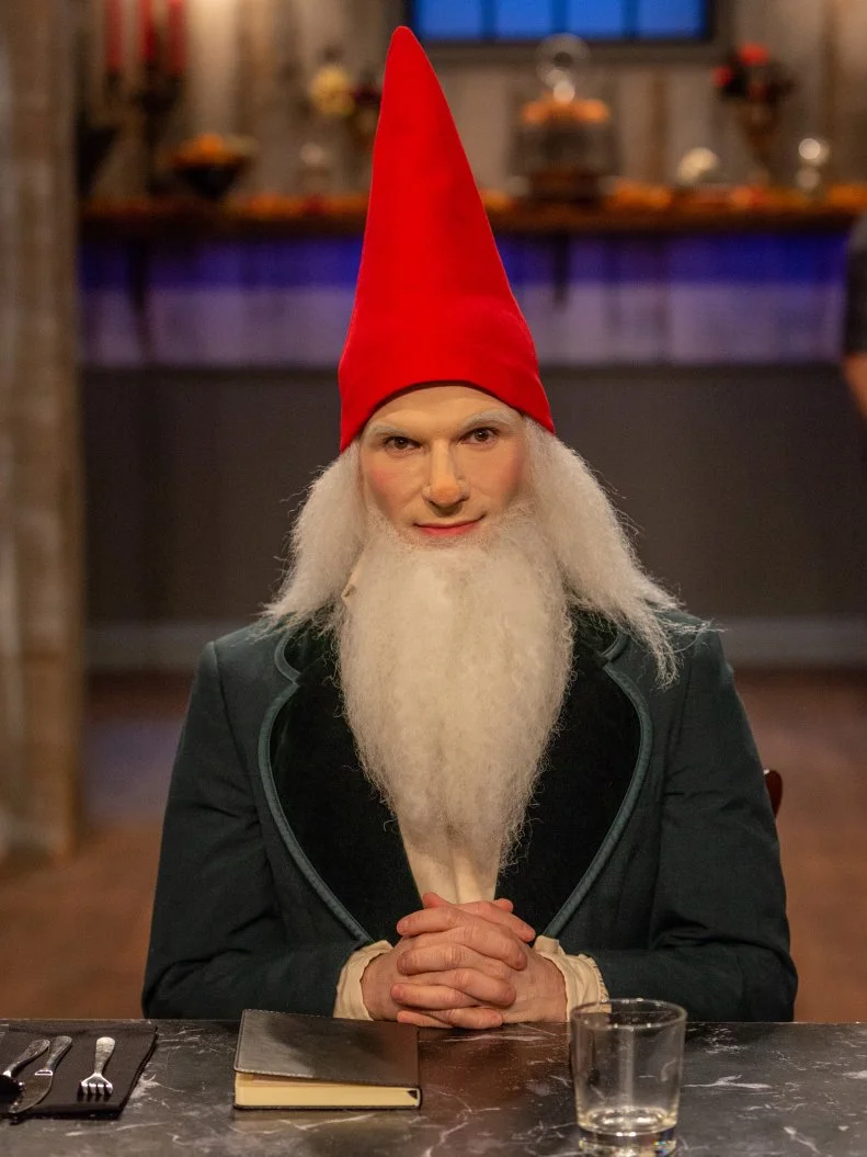 Judge Zac Young at the judges table in his gnome costume, as seen on Food Network's Halloween Baking Championship Season 4.