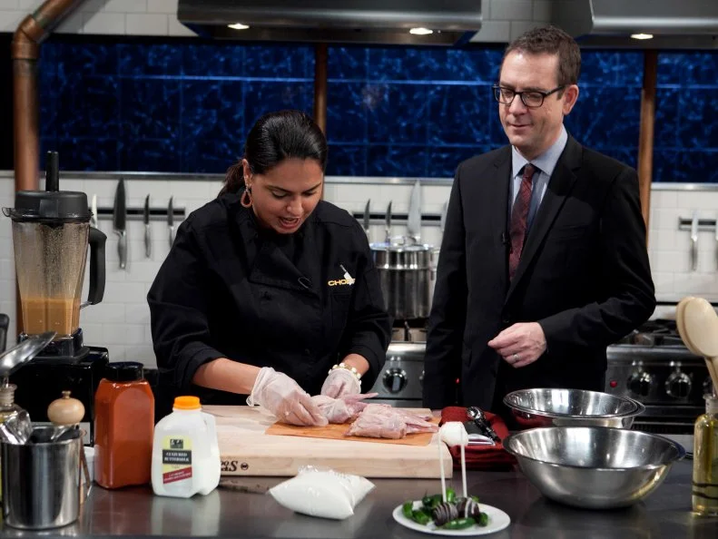 Chopped: After Hours host Ted Allen talks with chef Maneet Chauhan while she works on her entree that must include: Chocolate cake pops, white chocolate cocoa mix, quail and Serrano peppers, as seen on Food Network's Chopped: After Hours.
