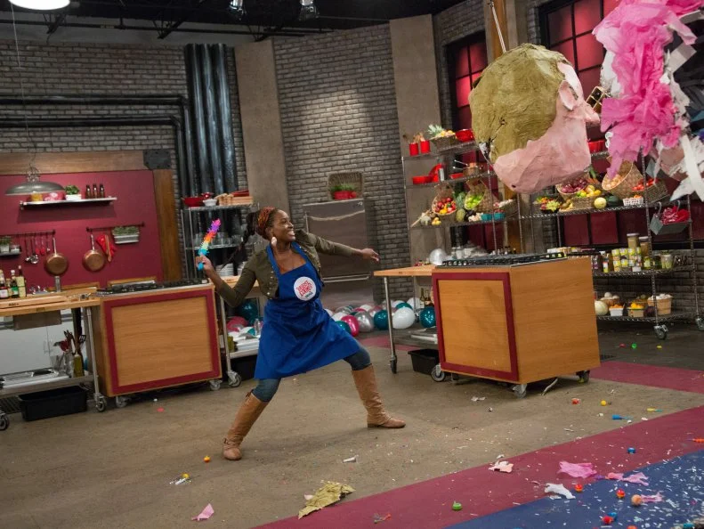 Blue Team member Stephanie St. Aubin takes a turn batting the pinata of Blue Team Leader Chef Bobby Flay, in the Surprise Party Challenge. Each team member must infuse the dishes they make for the surprise party, demonstrated for them by Blue Team Leader Chef Bobby Flay and Red Team Leader Anne Burrell, with the individual candy flavor each gets, and has to guess, when they burst giant pinata replicas of the chefs' heads, as seen on Food Network's Worst Cooks in America, Season 5.