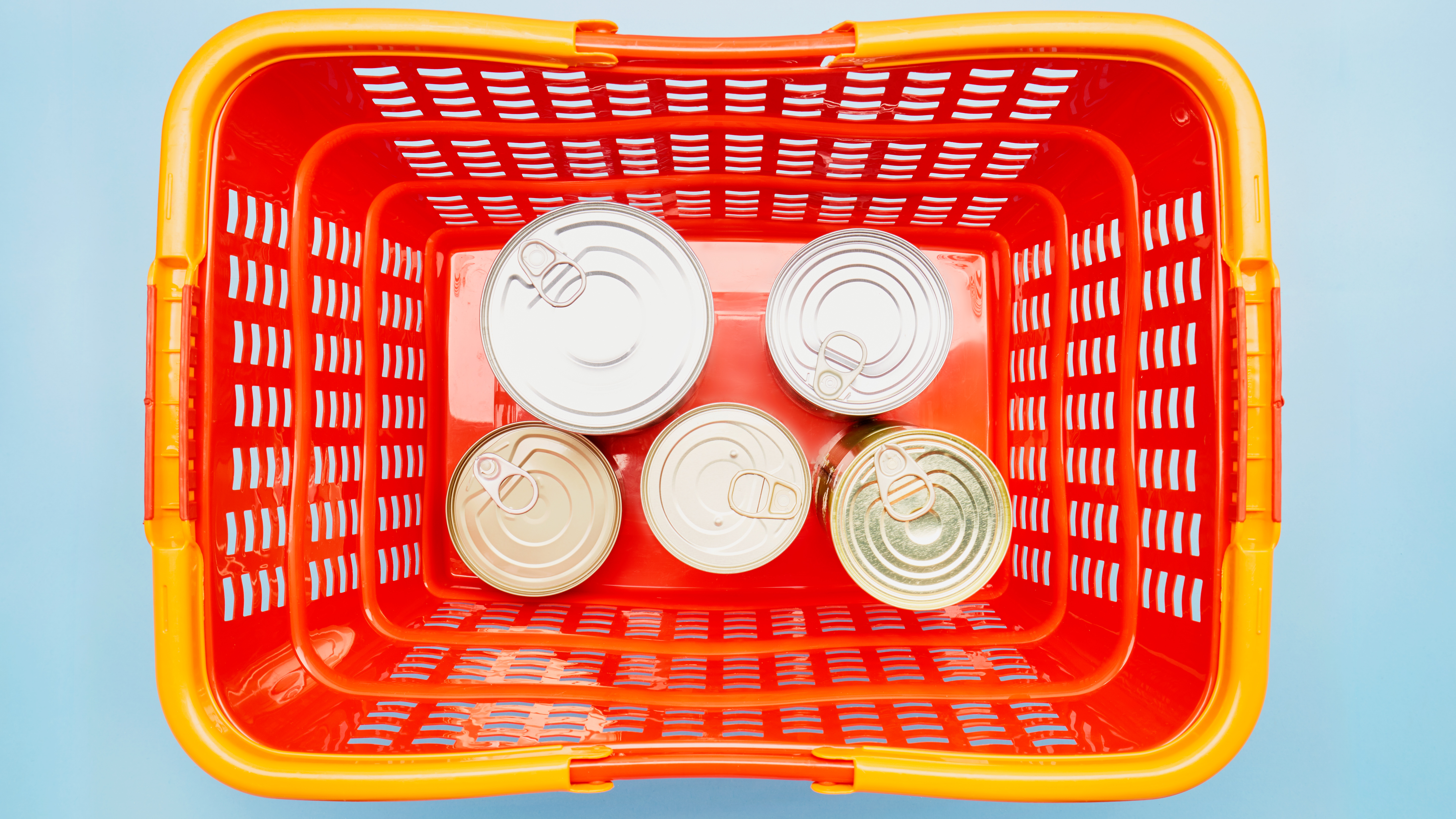 Still life of canned food in red shopping basket on blue background