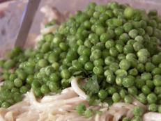 Giada adds thawed peas and parsley to the top of her fettucini dish. All the ingredients will get mixed toghether and put into a casserole dish to bake in the oven until the top is golden brown.