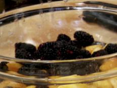 Blackberries are mixed with peaches in a glass bowl.