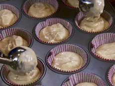 Cupcake batter is scooped into lined muffin tins.
