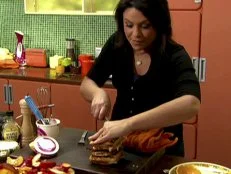 A woman uses a knife to slice through a savory waffle and chicken dish that is built like a sandwich. There is also bacon and rosemary maple gravy on this dish that is known as chicken and bacon wafflewiches.